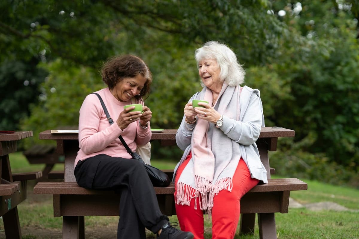 Two friends sharing coffee and conversation on a garden bench.
